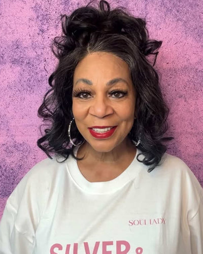 Soul Lady Wigs| Confident woman modeling a dark salt and pepper body wave wig by Soul Lady Wigs, featuring soft curls and a natural gray blend for a timeless, elegant style.
